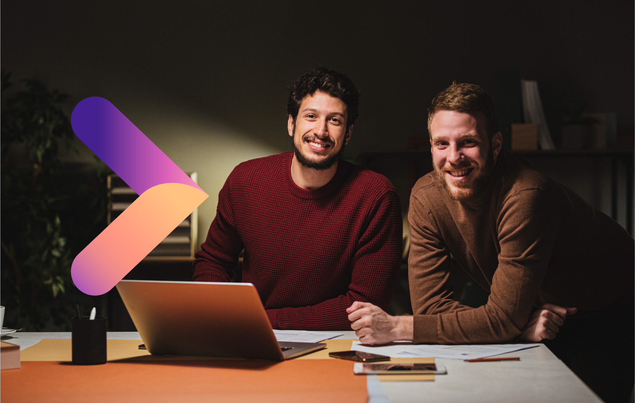 Two men sitting at laptop with brand arrow