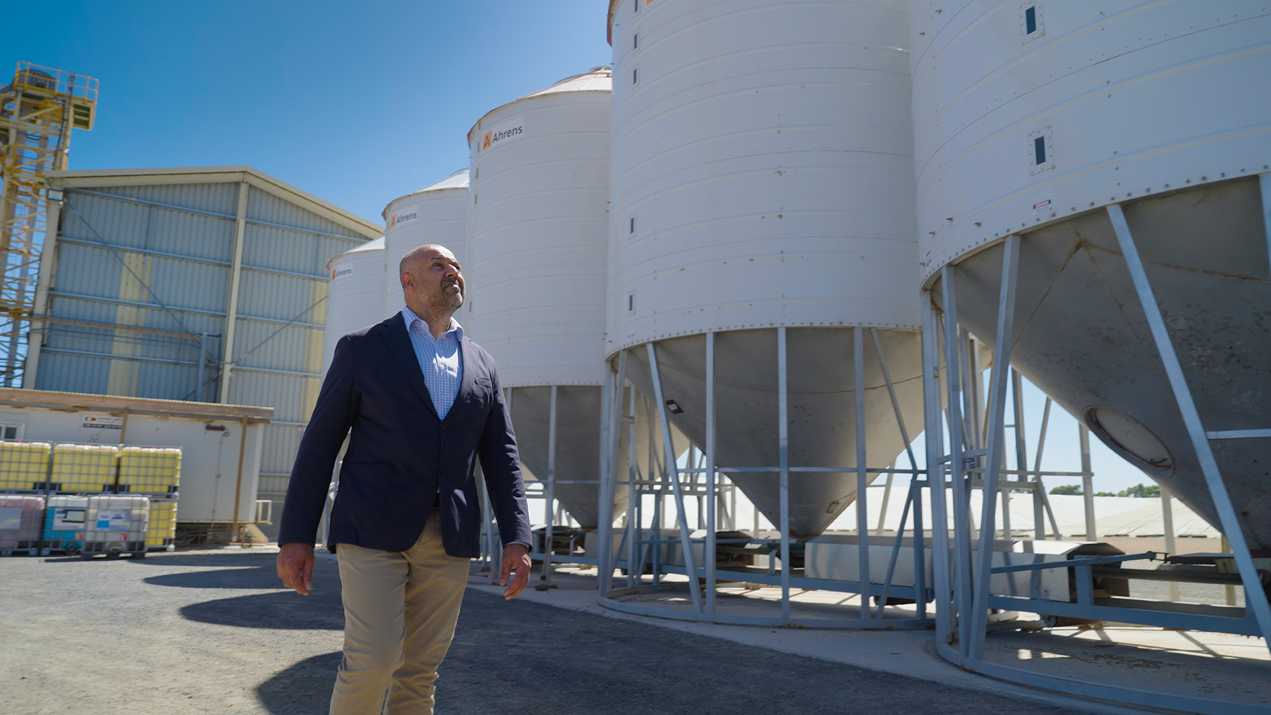Professor Harpinder Sandhu walking on farm with silos in background